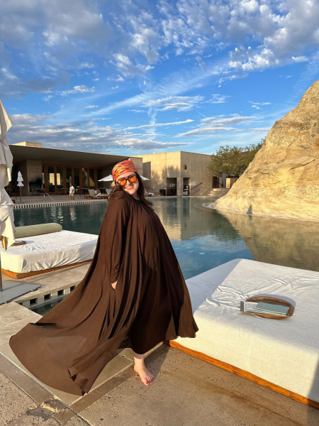 A photograph of Dianna Mazzone Singh wearing a black caftan and headscarf standing alongside a swimming pool.
